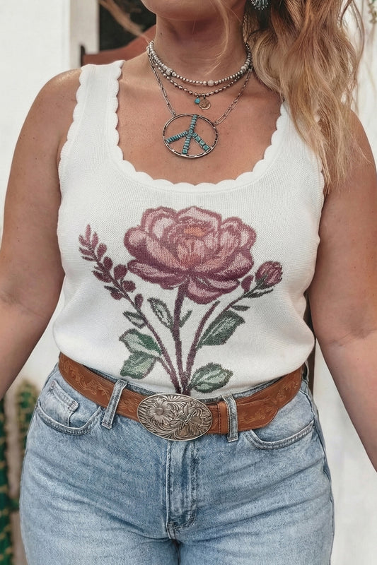 Person wearing a white tank top with a floral design and blue jeans.