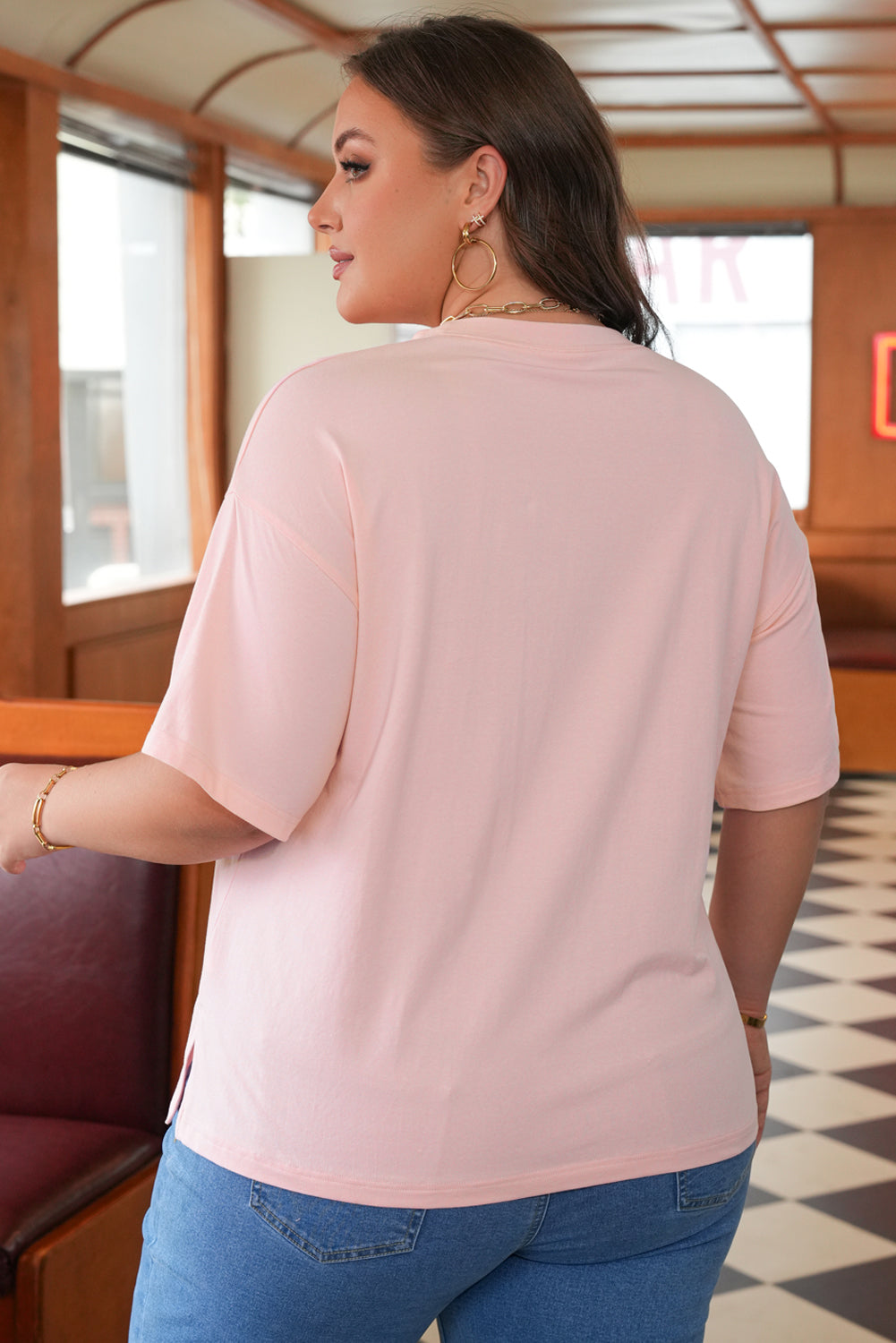 Woman wearing a light pink top and blue jeans in an indoor setting.